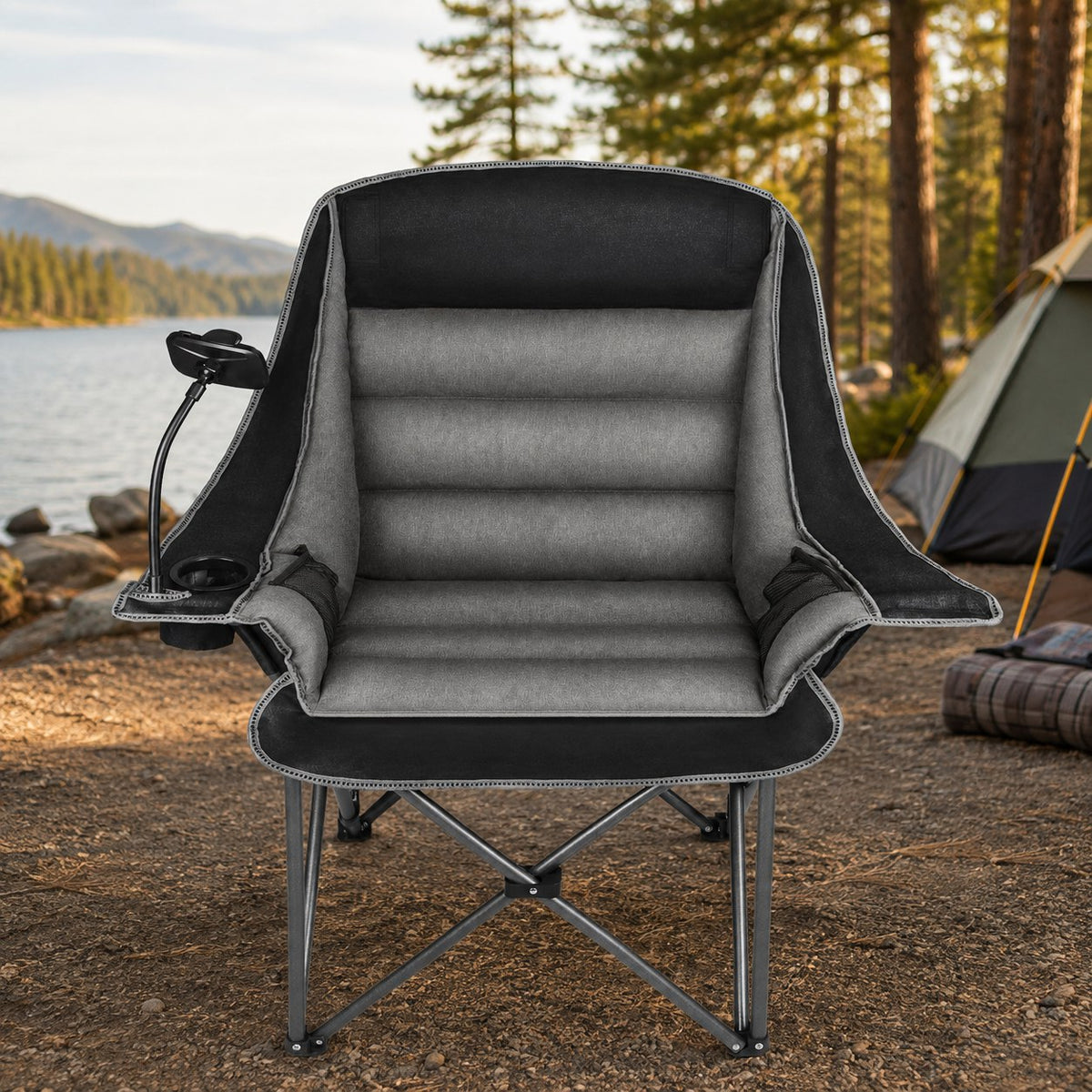 Front view of an oversized black and gray folding camping chair opened at a lakeside campsite