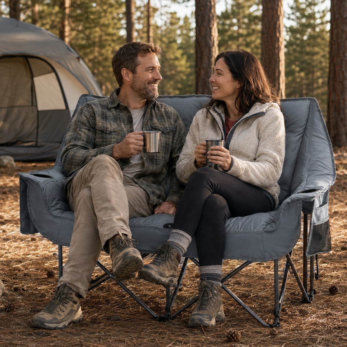 Couple relaxing in a gray padded double camping loveseat at a pine forest campsite