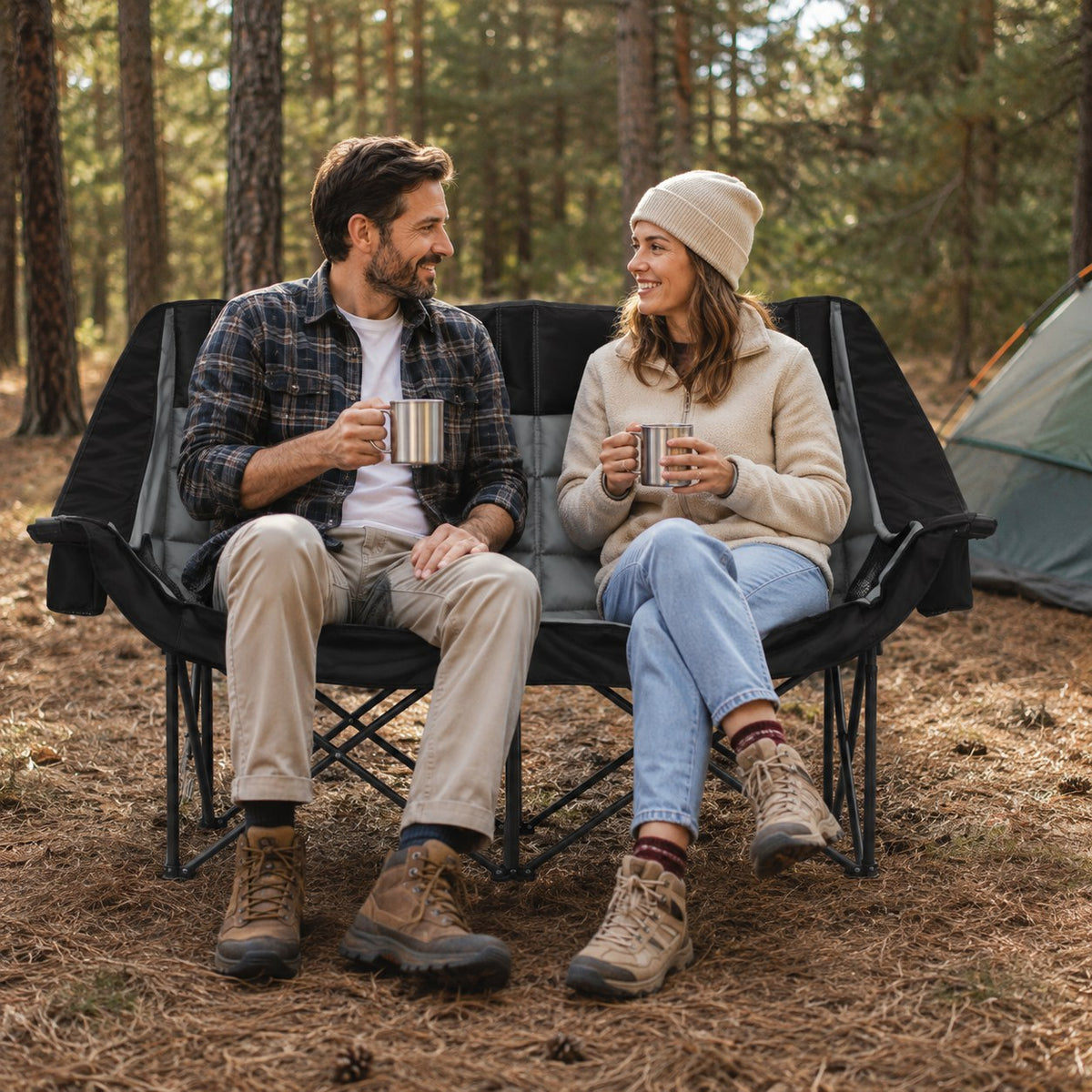 Couple relaxing together in a padded black and gray double camping chair at a pine forest campsite