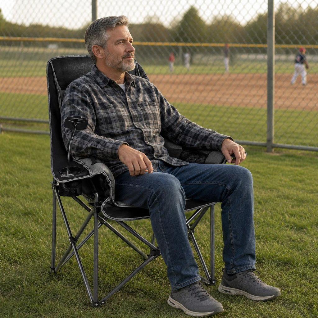 Adult relaxing in an oversized folding camping chair beside a community baseball field